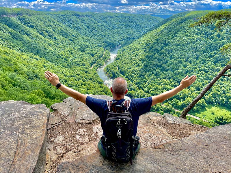 Steve sitting on the rocks at the  Endless Wall Overlook looking down at the New River.   